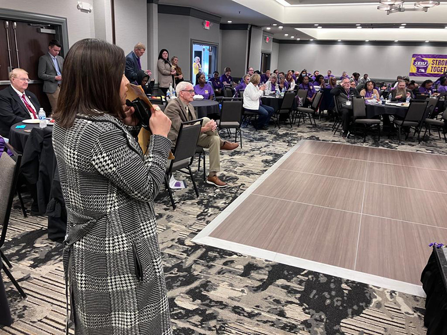 photo of an intrepreter at work at at conference. The interpreter is in the foreground and panelists and attendees are in the background