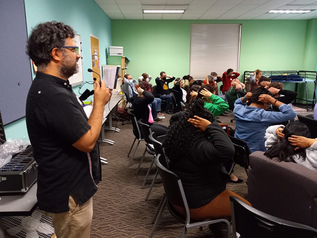 a photo of an interpreter interpreting a breakout group. The interpreter is at the back of the group and speaking into a microphone that is broadcast to headsets worn by the attendees